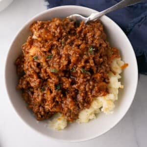 A bowl of mashed potatoes and ground beef with a spoon in the bowl.