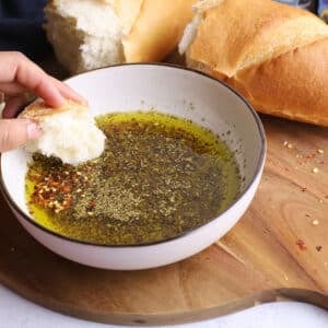 A hand holding some crusty bread dipped in a bowl of the dip recipe.