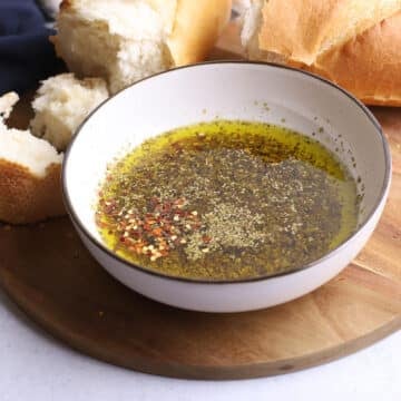 A white bowl with olive oil bread dip on a wooden board.