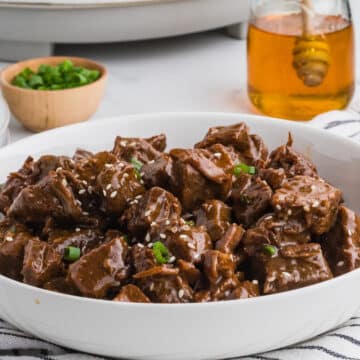 A white bowl with steak bites garnished with sesame seeds.