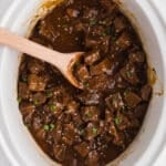 White slow cooker with steak bites and a spoon.