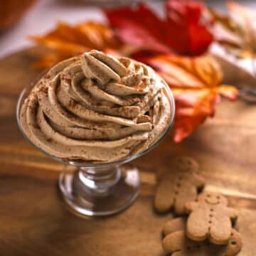 A clear wide glass filled with pumpkin cream and dusted with some cinnamon.