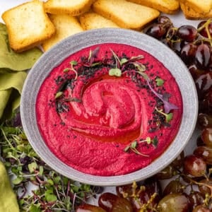 A close up image on a bowl with beet hummus garnished with greens.