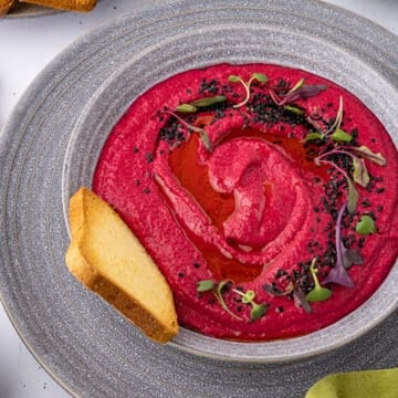 Beetroot hummus in a bowl garnished with seeds.