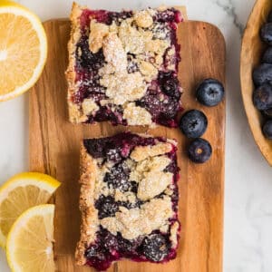 Blueberry lemon bars on a wooden cutting board with lemon slices.