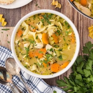 A white bowl of chicken noodle soup on a wooden surface.