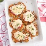 An overhead image of a white casserole dish with chicken parmesan thighs garnished with basil.