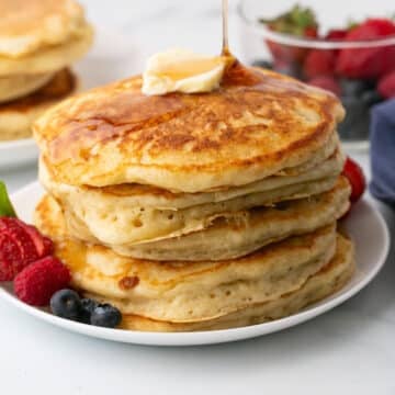 A stack of cracker barrel pancakes on a plate with fruits.