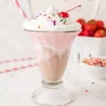 A tall glass cup with Neapolitan milkshake with a straw in the cup.