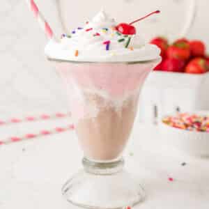 A tall glass cup with Neapolitan milkshake with a straw in the cup.