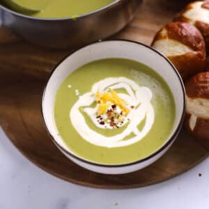 An overhead image of a bowl with asparagus soup on a wooden board.