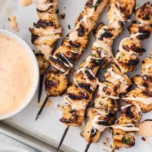 Sheet pan with grilled chicken skewers drizzled with bang bang sauce.