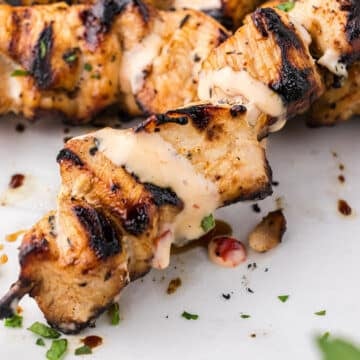 A zoomed in image on a chicken skewer garnished with sauce and parsley.