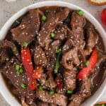 An overhead image of a white plate with mongolian beef garnished with sesame seeds.