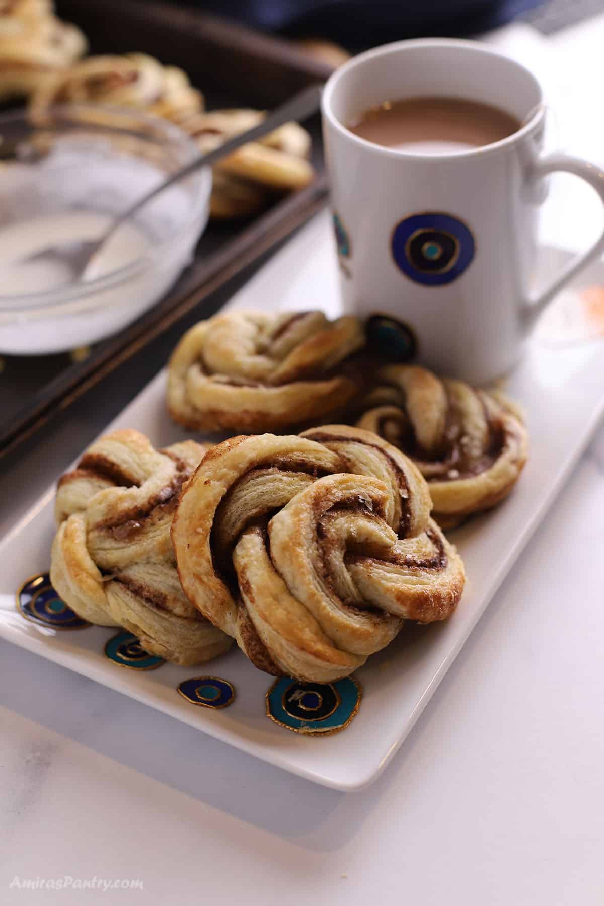 A long plate with cinnamon swirls with a cup of coffee.