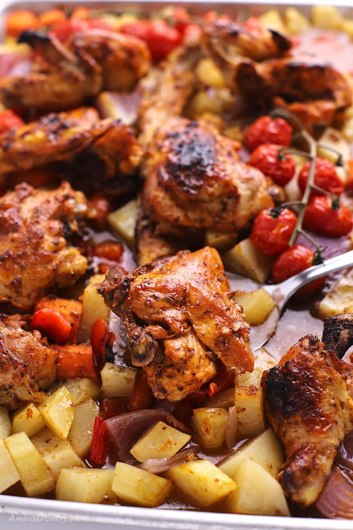 A sheet pan chicken with vegetables and a spoon in it.