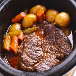 An overhead image of a black crockpot with pot roast and vegetables.