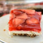 A close up image on a piece of strawberry pretzel salad on a white small plate.
