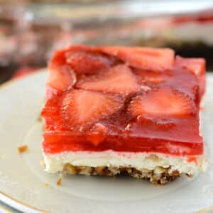 A close up image on a piece of strawberry pretzel salad on a white small plate.