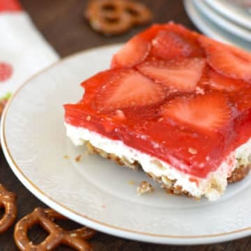 A square of strawberry pretzel salad in a whie plate on a wooden board.