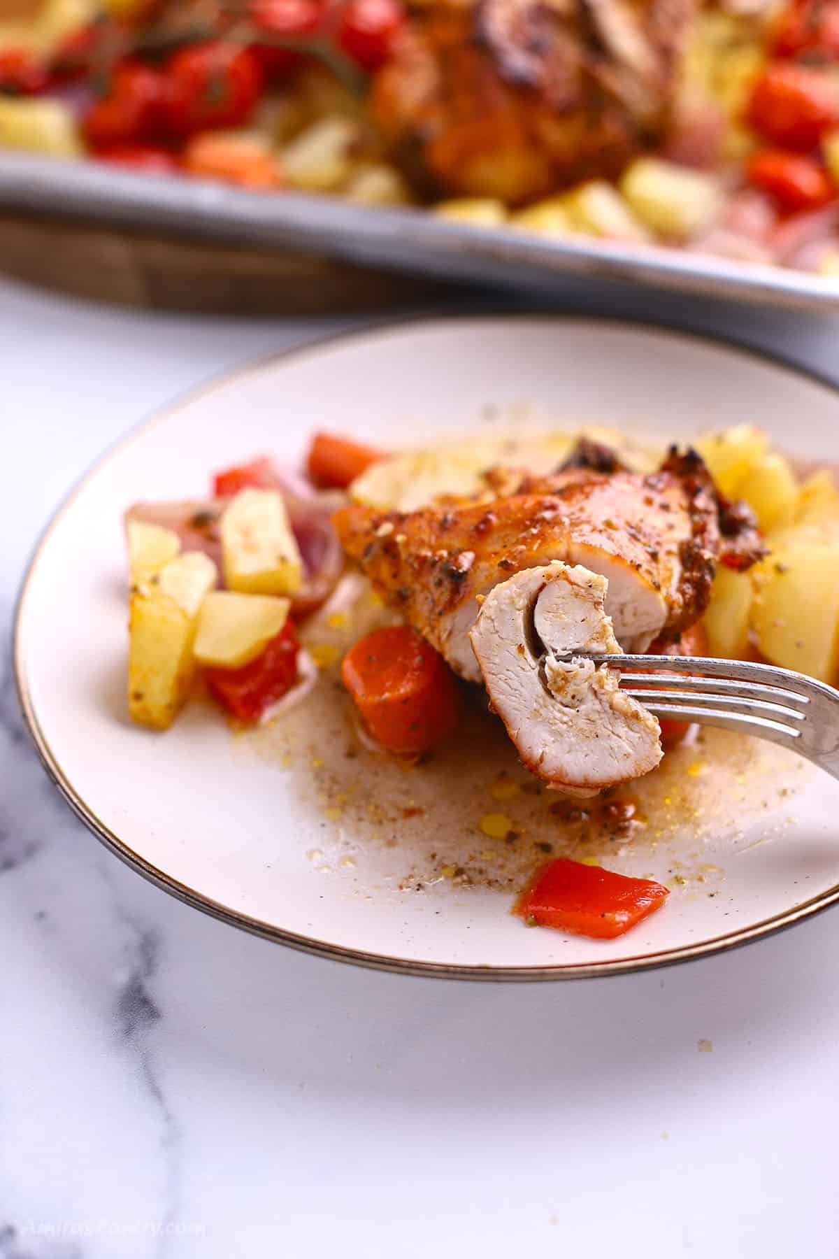 A fork with a piece of chicken from the sheet pan recipe.