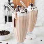 Two glasses with coffee milkshake topped with whipped cream.