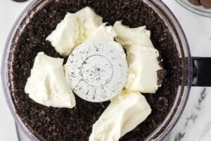 An overhead image of cream cheese and crushed cookies in a food processor.