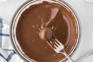 A cookie ball being left with a fork from a bowl of melted chocolate.