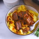 A white bowl with beef cubes on egg noodles.