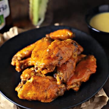 A close up image of buffalo chicken wings on a black plate.