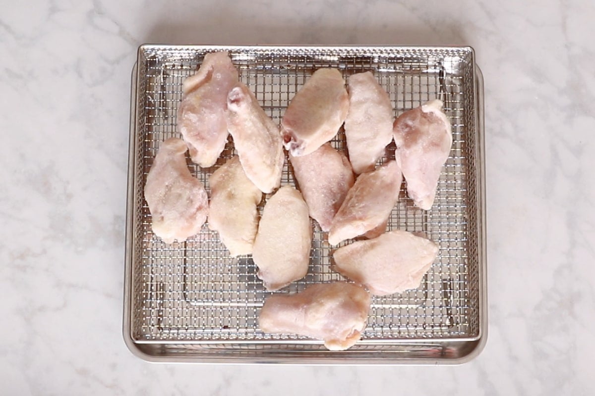 Frozen wings in an air fryer basket.