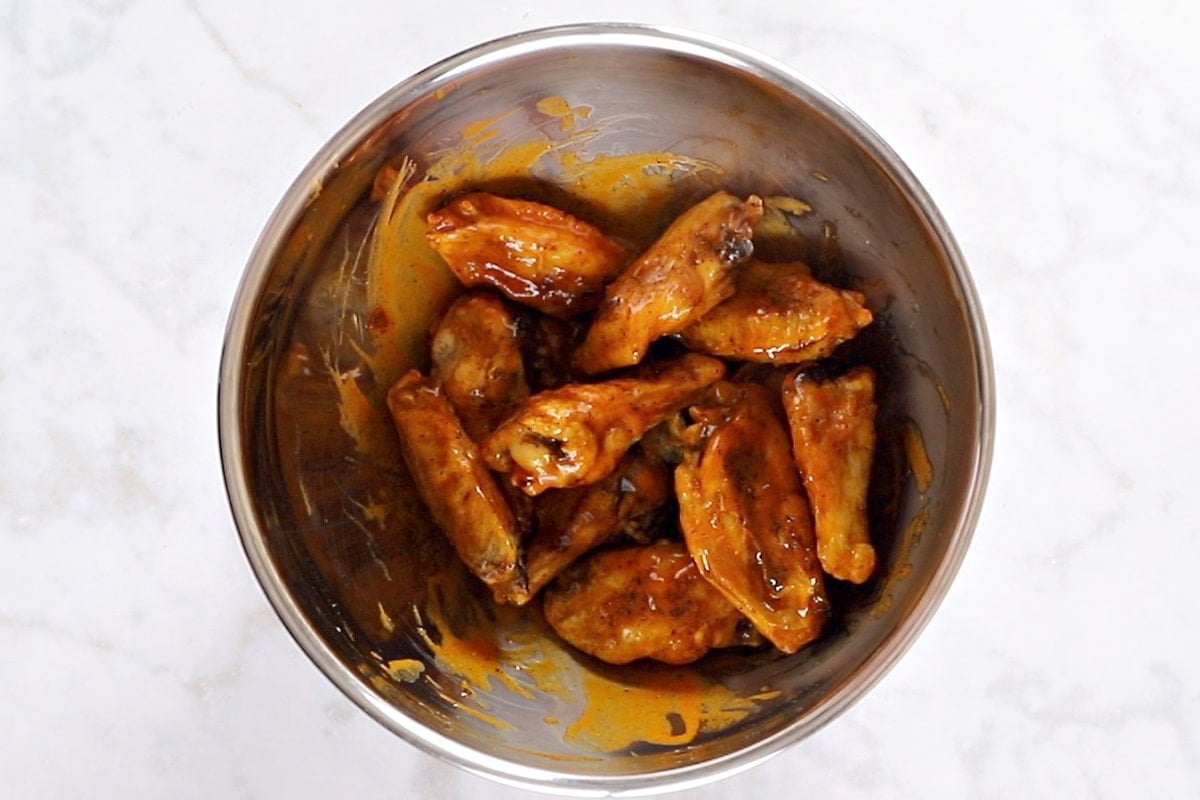 Air fried wings in a large bowl tossed with buffalo sauce.