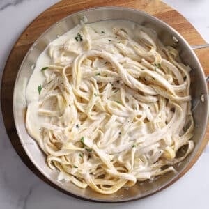 An overhead image of a large skillet with pasta with Alfredo sauce with half and half.