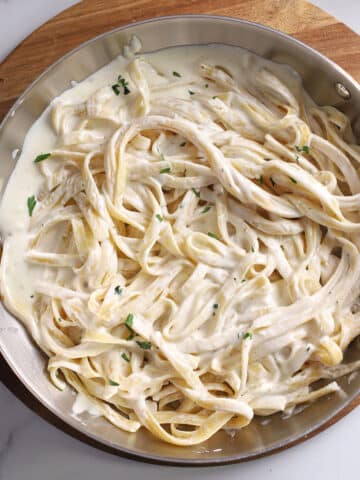 An overhead image of a large skillet with pasta with Alfredo sauce with half and half.