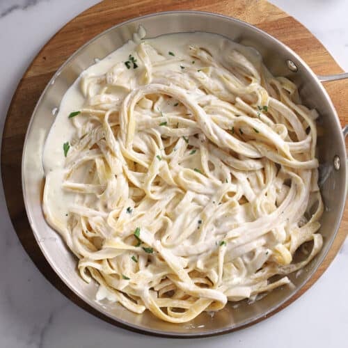 An overhead image of a large skillet with pasta with Alfredo sauce with half and half.