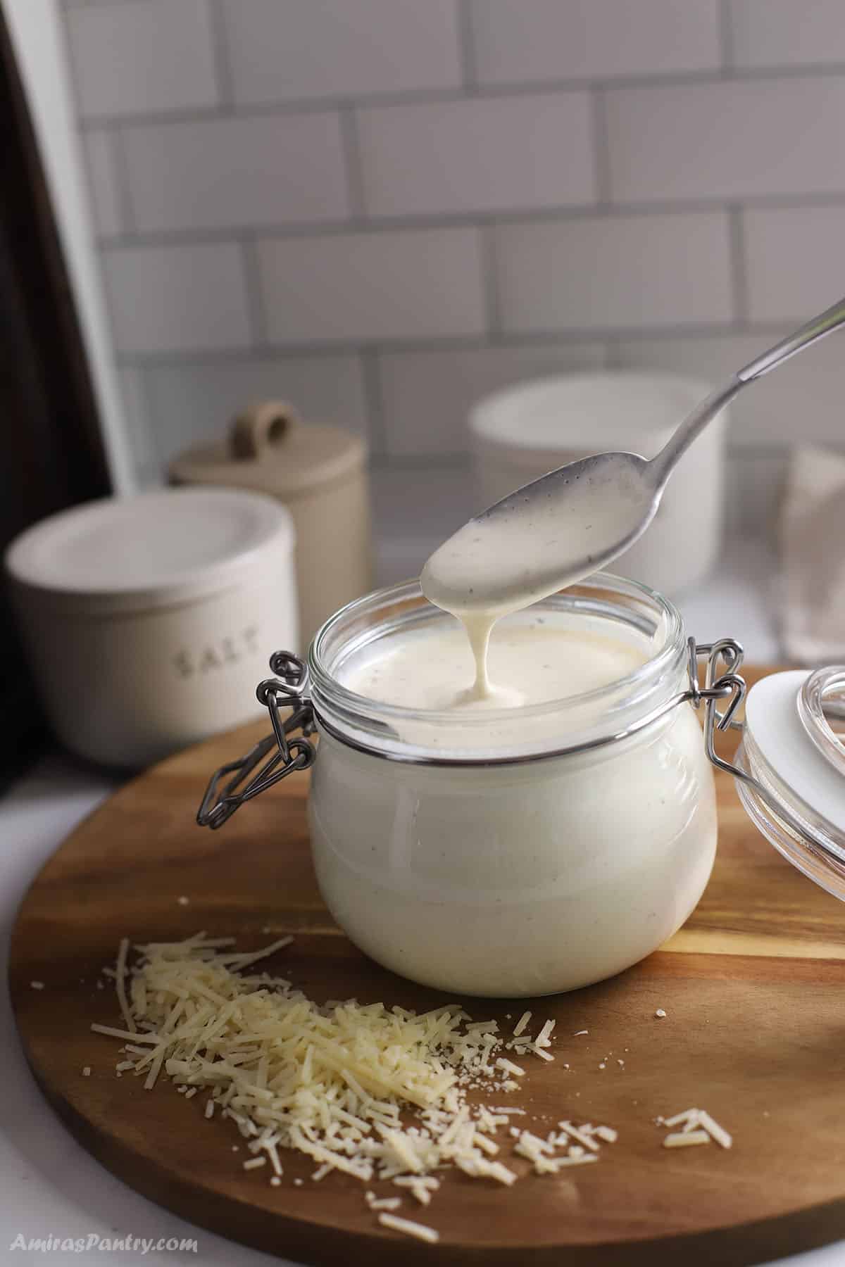 A spoon scooping some sauce out of a jar with alfredo sauce made with half and half.