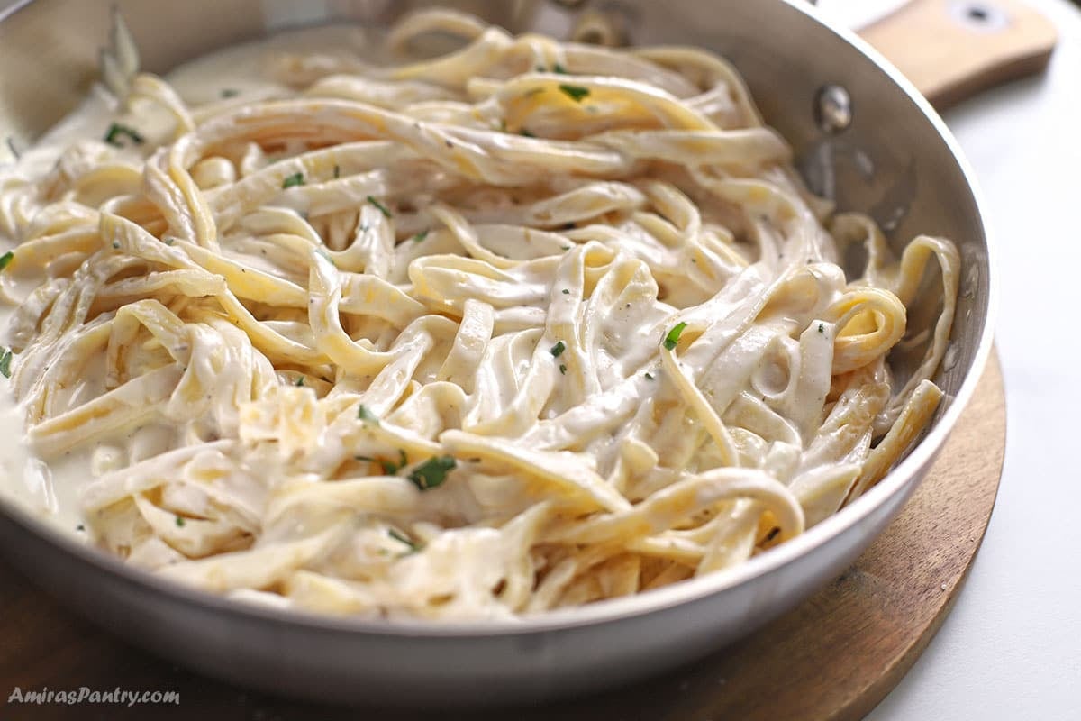 A skillet with Alfredo fettuccine garnished with parsley.