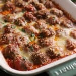Baked meatballs in a green ceramic casserole topped with melted cheese.