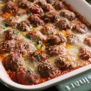 Baked meatballs in a green ceramic casserole topped with melted cheese.