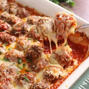 A serving spoon scooping some baked meatballs from a casserole dish.