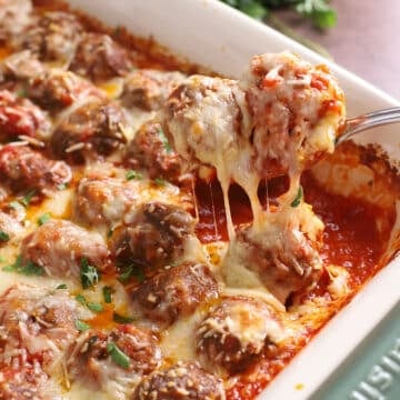 A serving spoon scooping some baked meatballs from a casserole dish.