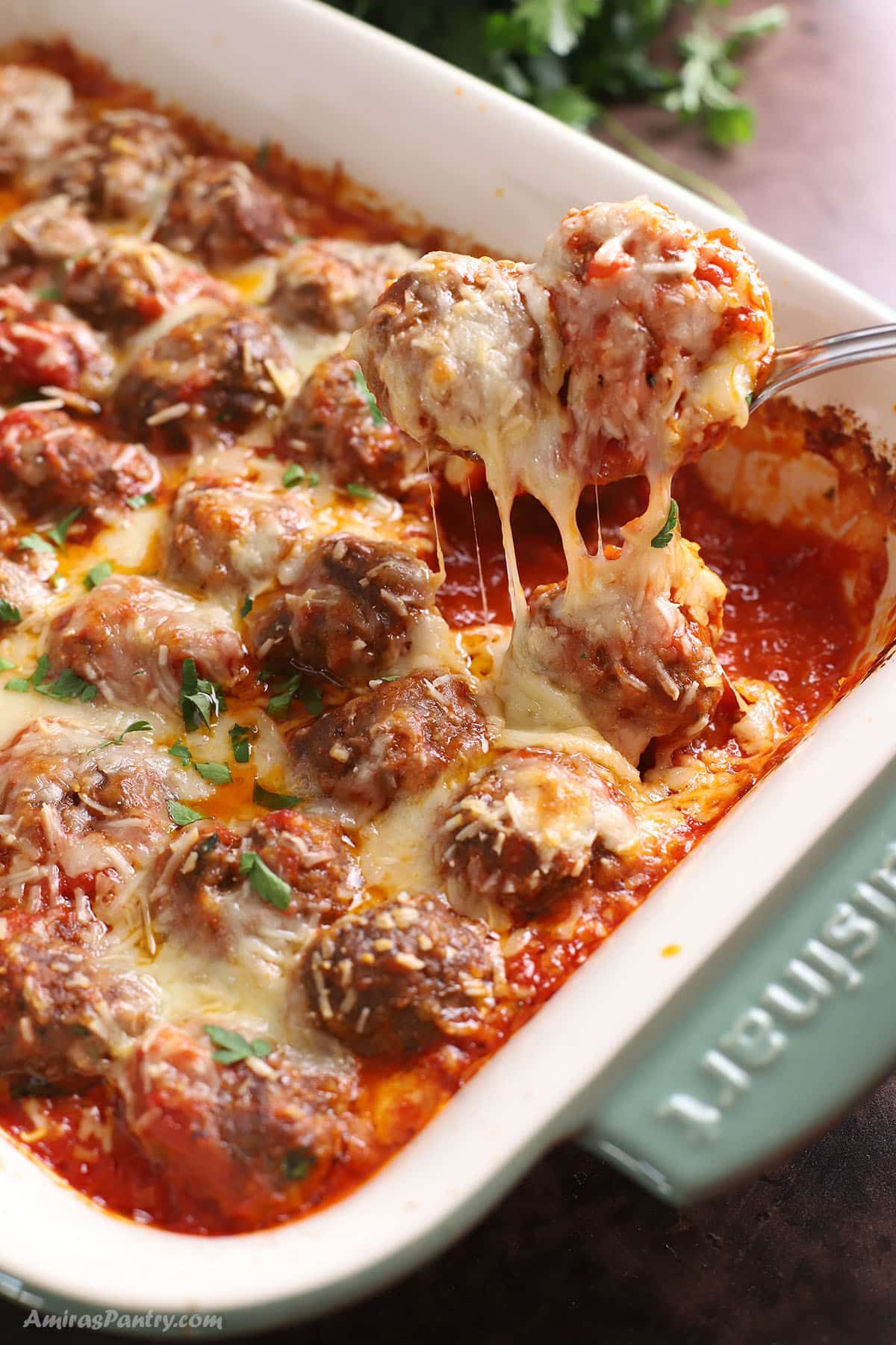 A green ceramic casserole with baked meatballs topped with melty cheese.