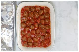 Partially baked meatballs on a 13x9 baking dish with marinara sauce.