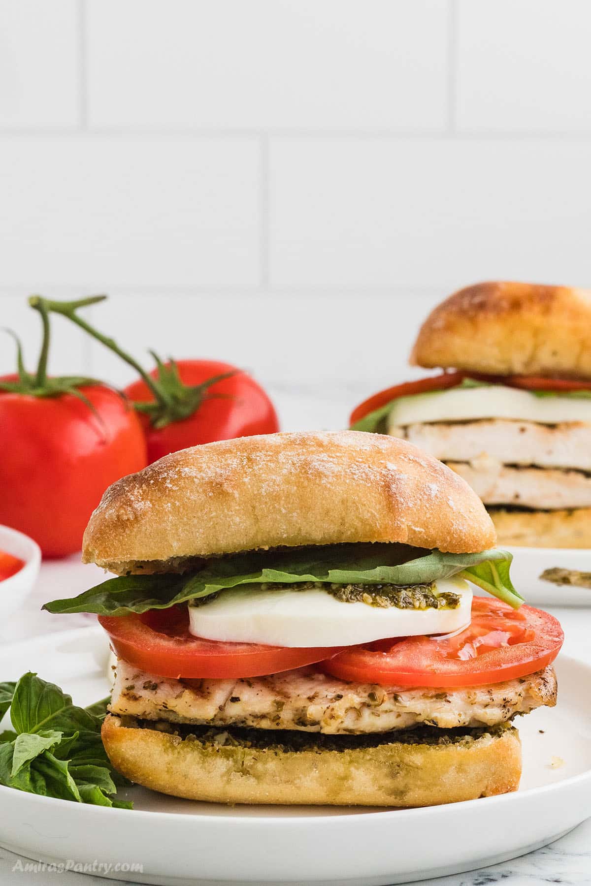 Chicken Caprese sandwich with tomatoes in the back.