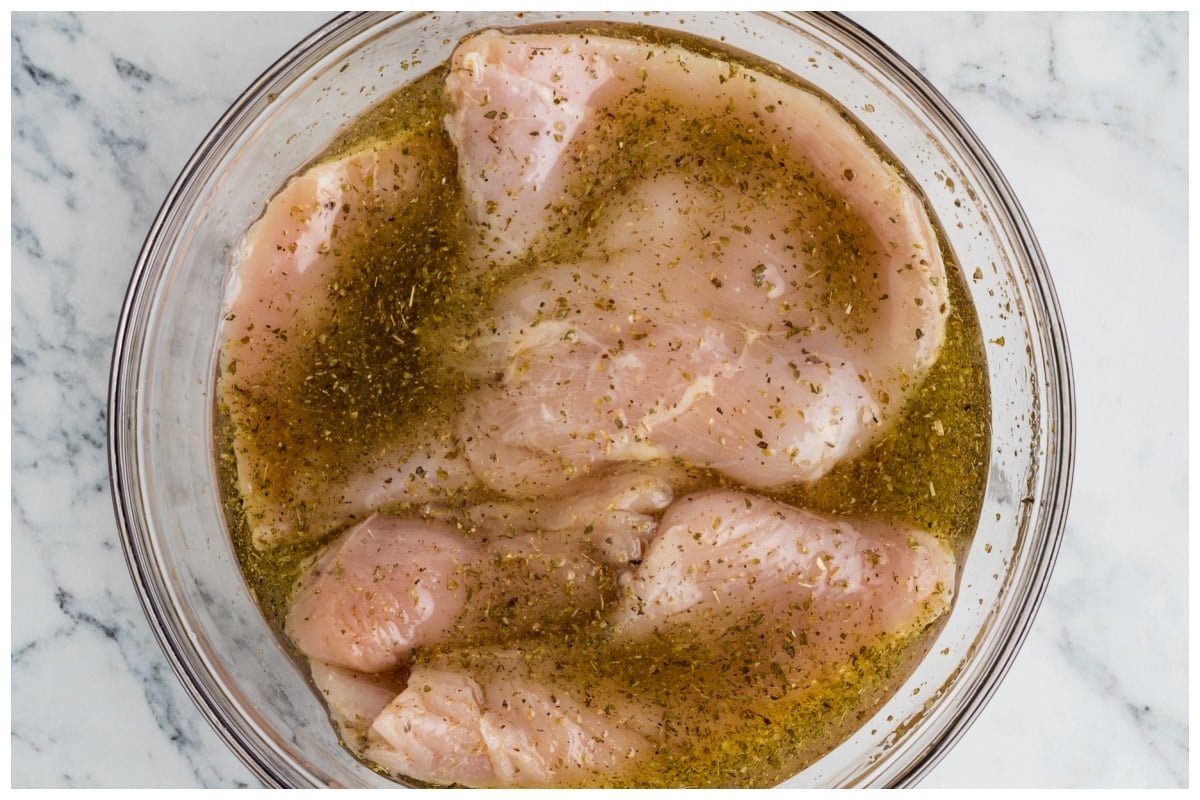 Chicken breasts marinated in a bog glass bowl.