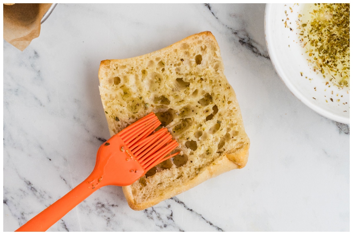 Brushing bread pieces with pesto.
