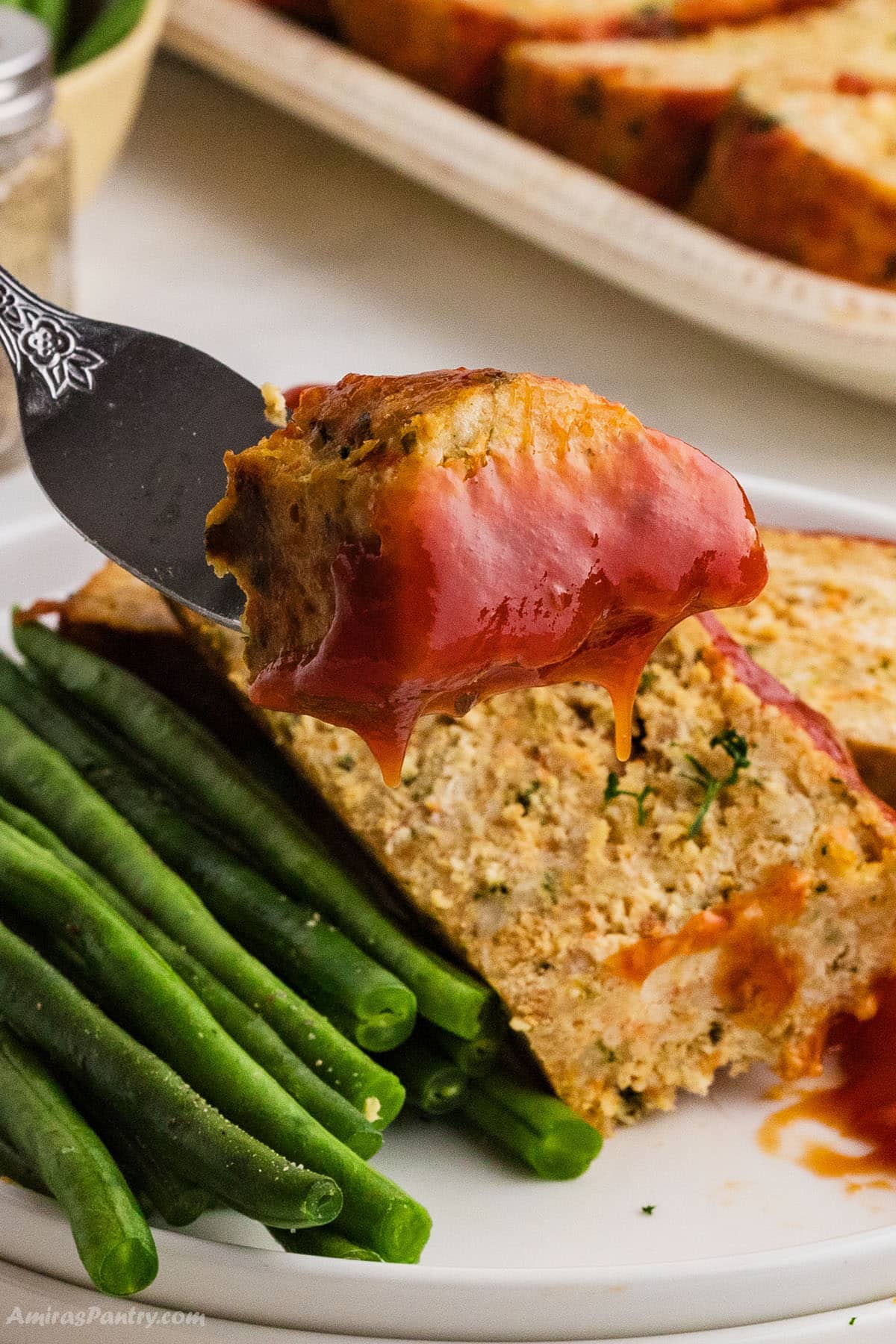 A fork with a piece of chicken meatloaf with sauce.