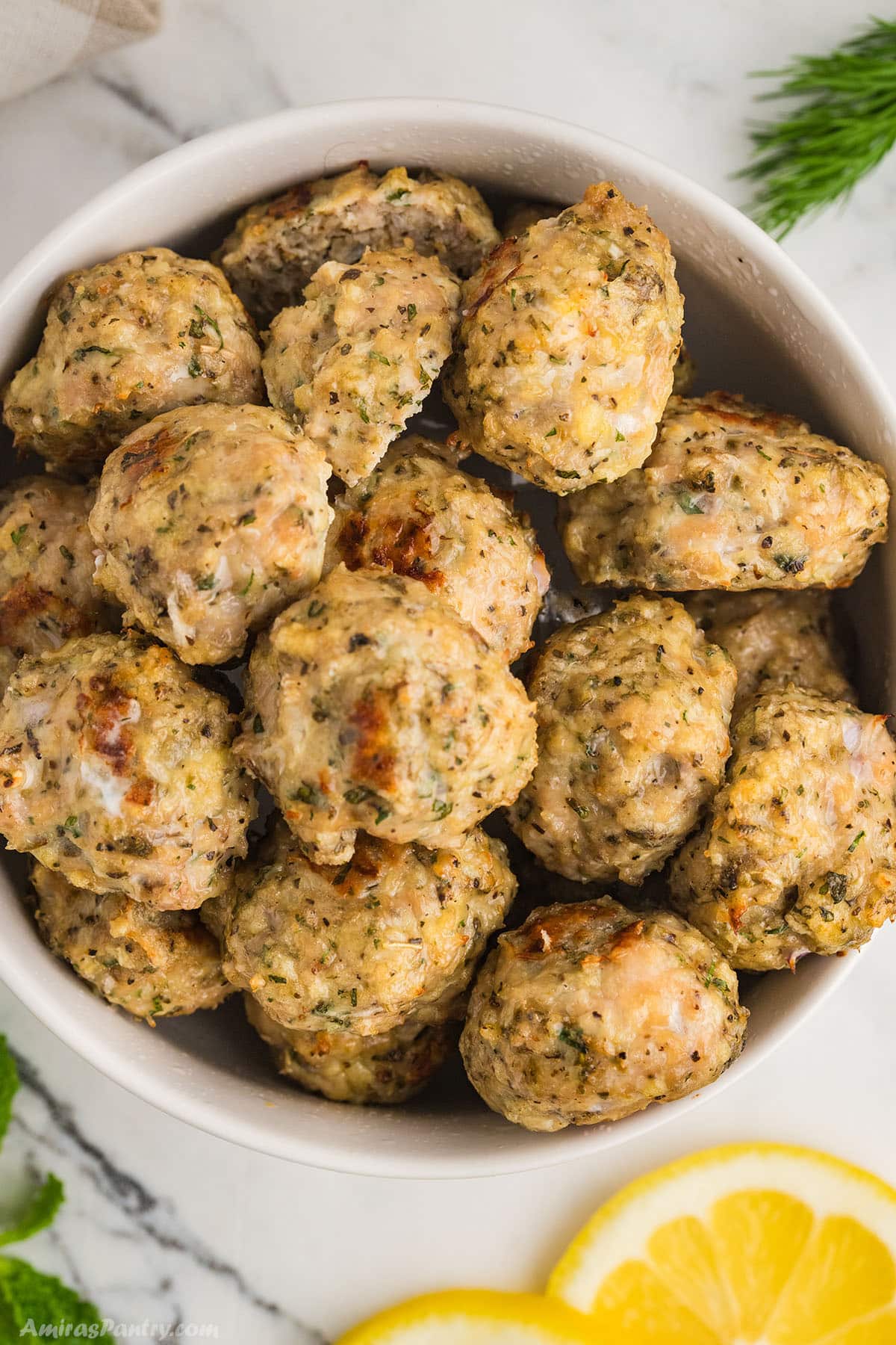A large bowl with chicken meatballs with lemon slices on the side.