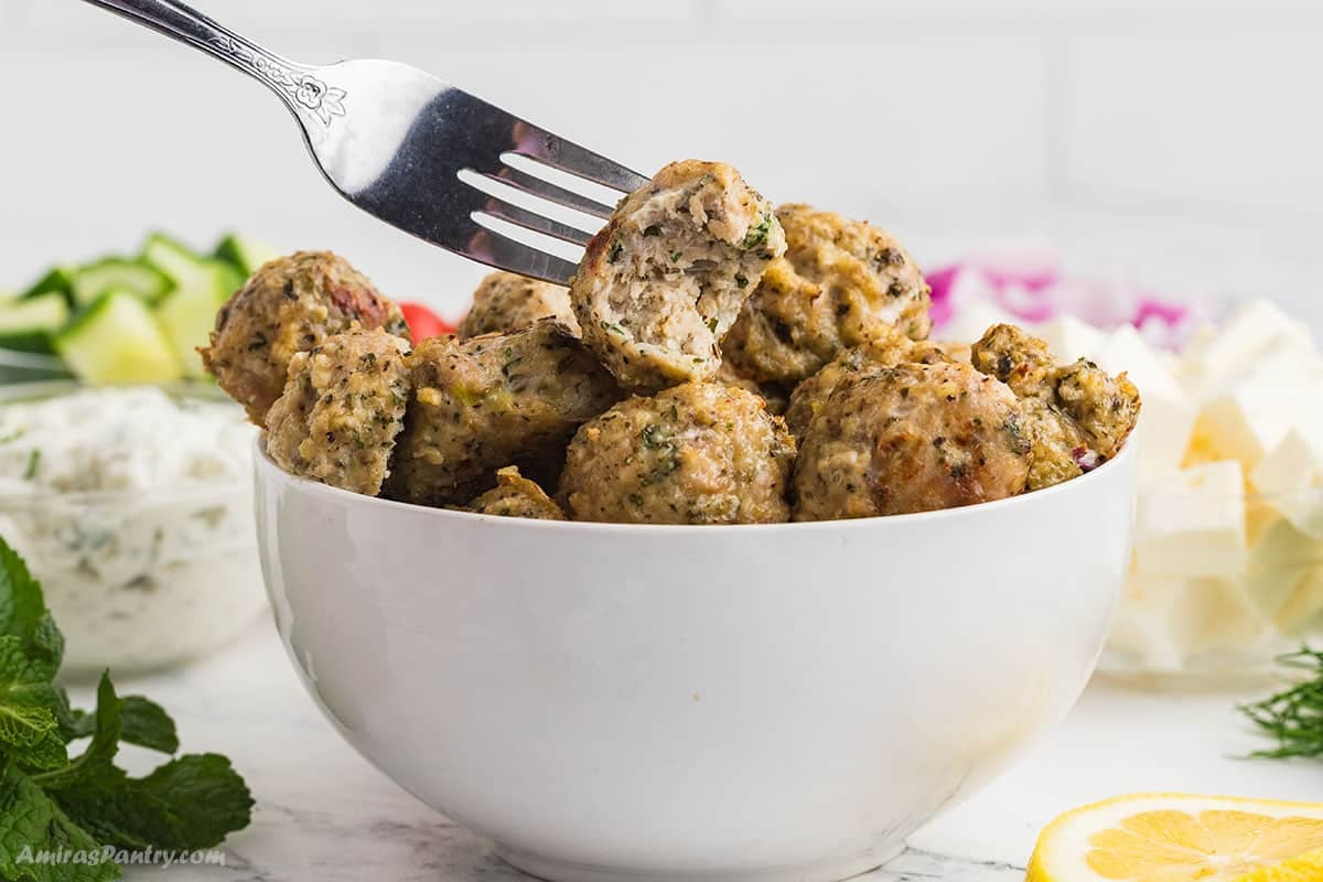 A fork holding one chicken meatball with a bite taken from it.