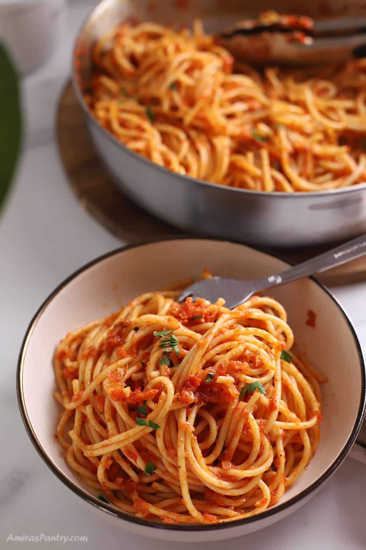 Harissa pasta in a small bowl with the whole skilletin the back.